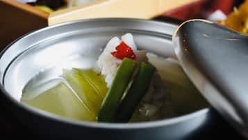 A bowl of soup with rice, green vegetables, and a red chili.
