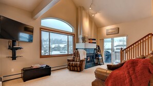 A living room with a fireplace, a large window, a flat-screen TV, and a staircase.