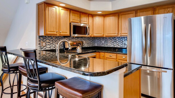 A modern kitchen with wooden cabinets, stainless steel appliances, and a black and white tiled backsplash.