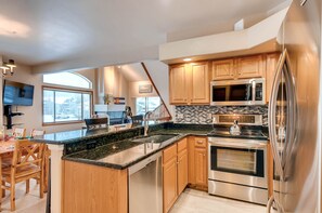 A modern kitchen with wooden cabinets, a stainless steel refrigerator, a built-in oven, and a granite countertop.
