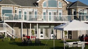 A large house with a covered patio area, multiple windows, and a staircase leading to the upper level. - water front luxury lake house (Janetville)