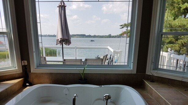 A bathroom with a large bathtub, a window with a view of a lake and dock, and a potted plant. - water front luxury lake house (Janetville)