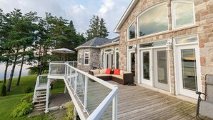 A stone house with a deck, a glass door, and a staircase leading to the deck. - water front luxury lake house (Janetville)