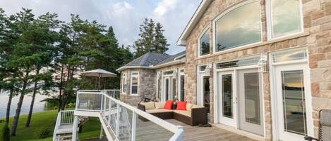 A stone house with a deck, a glass door, and a staircase leading to the deck.
