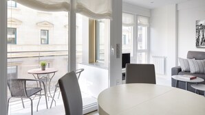 Uma sala de estar moderna com uma mesa redonda e cadeiras, um sofá e uma janela grande com vista para edifícios.