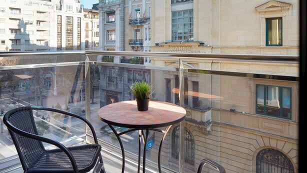 Varanda com uma mesa redonda e duas cadeiras, um vaso de planta e vista para edifícios históricos.