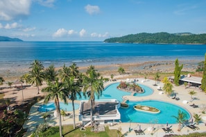 Un complexe hôtelier doté d’une grande piscine, de palmiers et offrant une vue sur la plage.