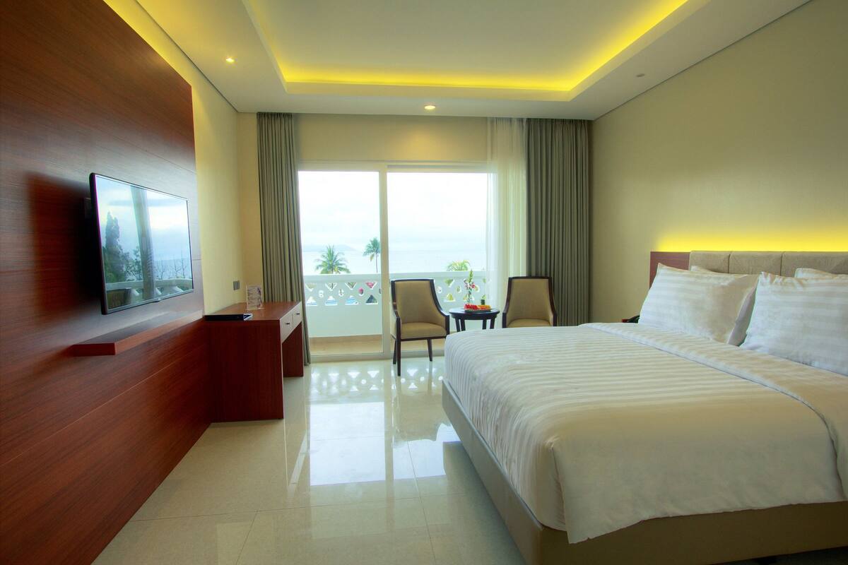 Une chambre d’hôtel avec un grand lit, un bureau, une chaise et un téléviseur fixé au mur.