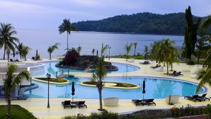 Een resort zwembadgedeelte met meerdere zwembaden, ligbedden en palmbomen.