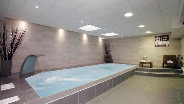 Un área de spa con una piscina rectangular, una cascada y una zona de estar con un banco y una mesita.