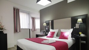 Habitación de hotel moderna con una cama grande, un escritorio con una computadora portátil, lámparas de noche y una mesita con un teléfono y una taza.