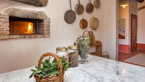 Una cocina con horno de leña, frascos de hierbas y ollas colgando.