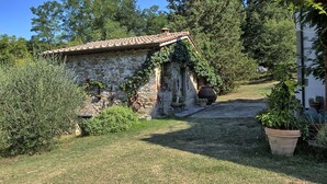Un edificio rústico de piedra con techo de tejas, rodeado de exuberante vegetación y un césped bien cuidado.