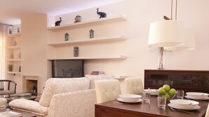 A living room with a sofa, dining table, chairs, and shelves with decorative items.