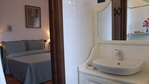 A bedroom with a bed, a bedside table, a nightstand, a mirror, and a bathroom with a sink and a mirror. - Villa il Castagno - Three Bedroom Villa, Sleeps 11 (Val Canina)