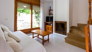 A room with a bed, a wooden table, a TV, a fireplace, and a staircase. - INNOUTHOME HOUSE WITH GARDEN AND SWIMING-POOL, BBQ AC AND WIFI,_JUAN DE ALMENARA (L'AMETLLA DE MAR)