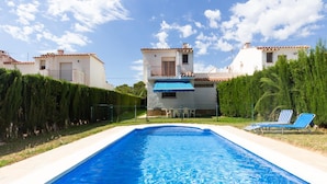 A swimming pool with two lounge chairs, surrounded by a hedge and a white building with a blue awning. - INNOUTHOME HOUSE WITH GARDEN AND SWIMING-POOL, BBQ AC AND WIFI,_JUAN DE ALMENARA (L'AMETLLA DE MAR)