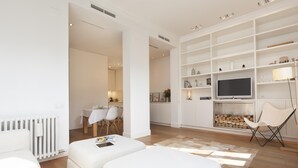 A modern living room with a sofa, ottoman, TV, and bookshelf.