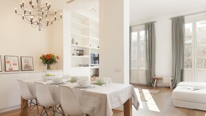 A modern living room with a dining area, a chandelier, and a large window with curtains.