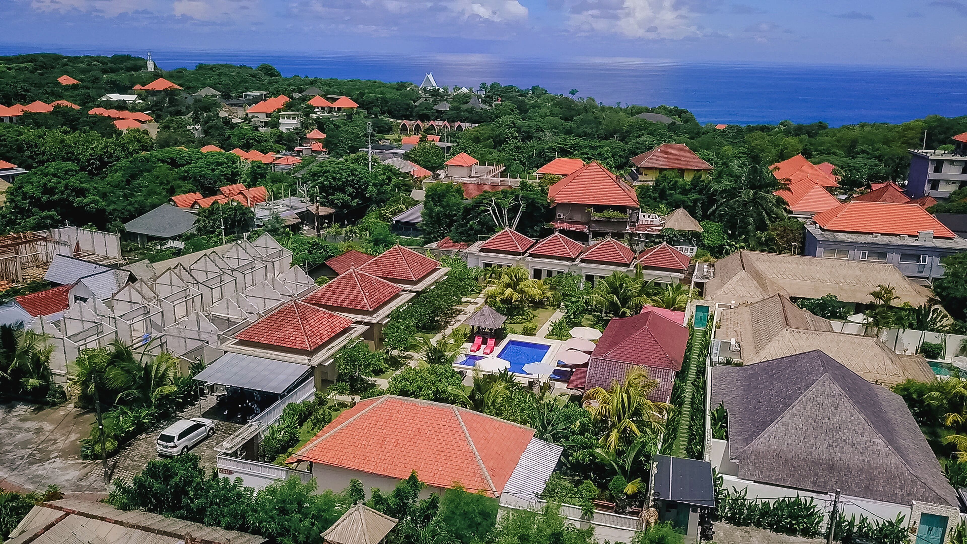 An aerial view of a residential area with red-roofed houses, a swimming pool, and a view of the ocean.