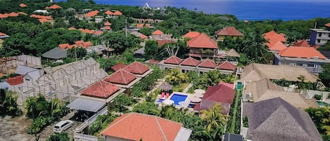 An aerial view of a residential area with red-roofed houses, a swimming pool, and a view of the ocean.