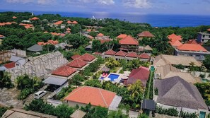 An aerial view of a residential area with red-roofed houses, a swimming pool, and a view of the ocean. - Uluwatu Jungle Villa (Pecatu)