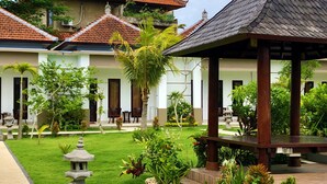 A traditional building with a tiled roof, a covered seating area, and a well-maintained garden with various plants and a stone lantern. - Uluwatu Jungle Villa (Pecatu)