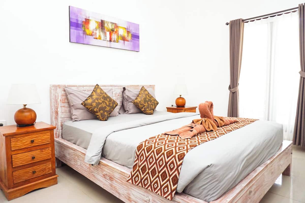 A neatly arranged bedroom with a bed, pillows, a bedside table, and a lamp.