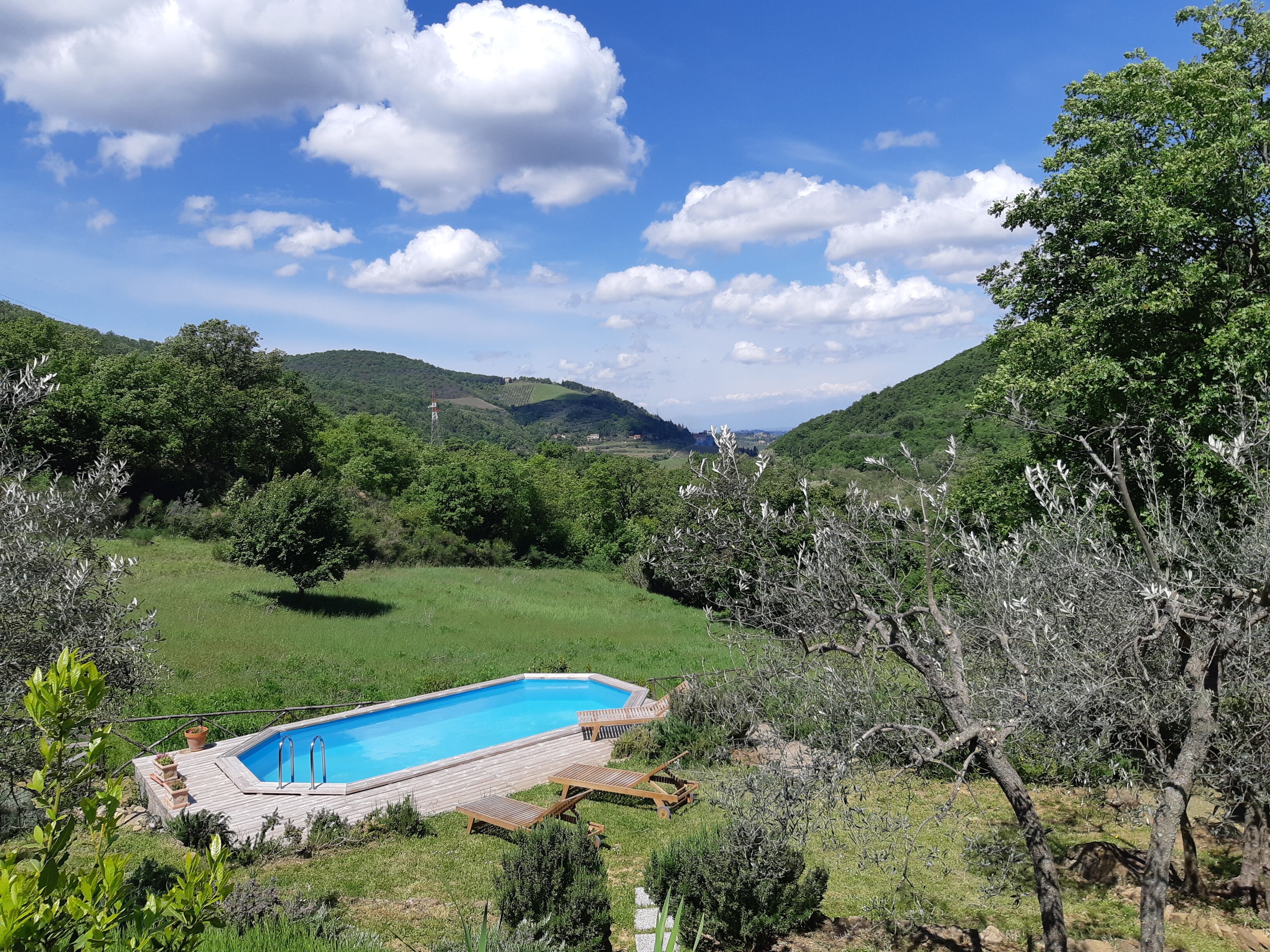 A swimming pool with wooden deck and lounge chairs, surrounded by greenery and hills.