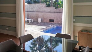 A modern room with a glass table and chairs, a view of an outdoor swimming pool, and a large window with curtains. - Private Villa with swimming pool & barbecue (Funchal)