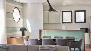 A modern living room with a sofa, a dining table with chairs, a kitchen area with cabinets, and a large window. - Private Villa with swimming pool & barbecue (Funchal)