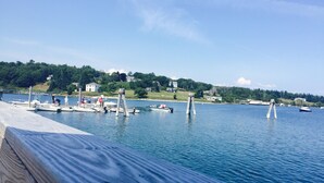 Margem com barcos atracados, um cais e vista para uma colina com casas.