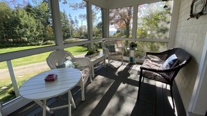 Varanda coberta com mesa, cadeiras, um sofá e vista para uma área gramada e árvores.