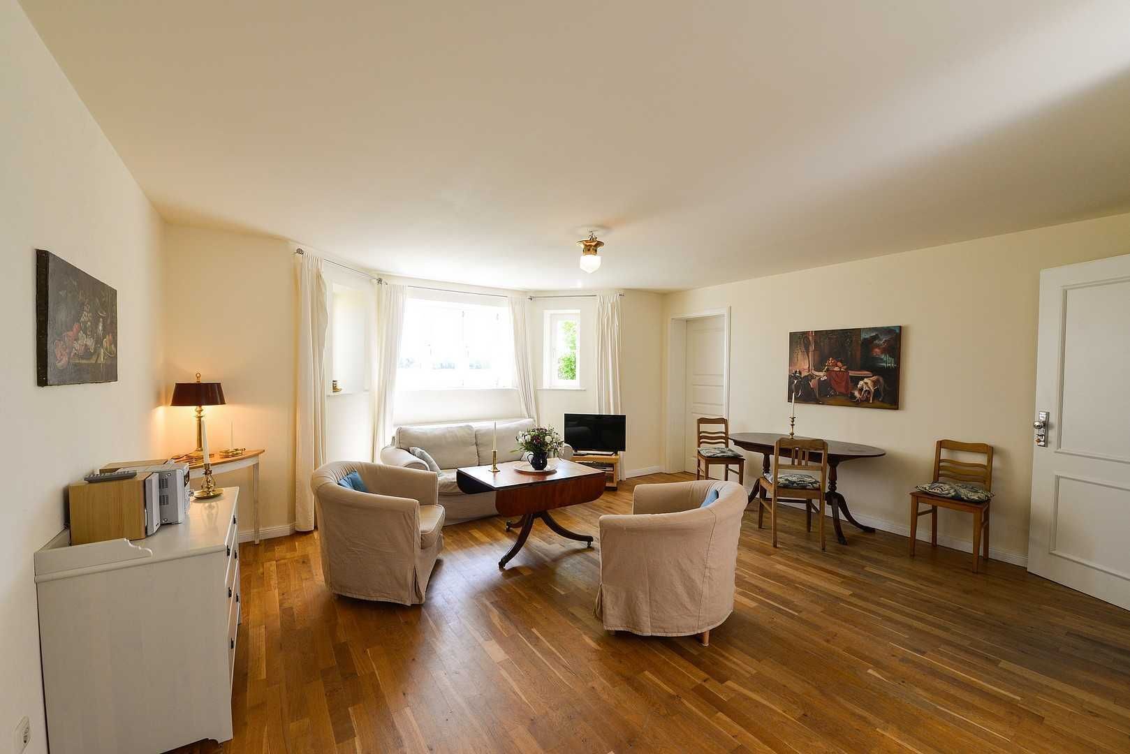 Un salon spacieux doté d’un plancher en bois, d’un canapé, de deux fauteuils, d’une table basse, d’un téléviseur et d’une table à manger avec des chaises.