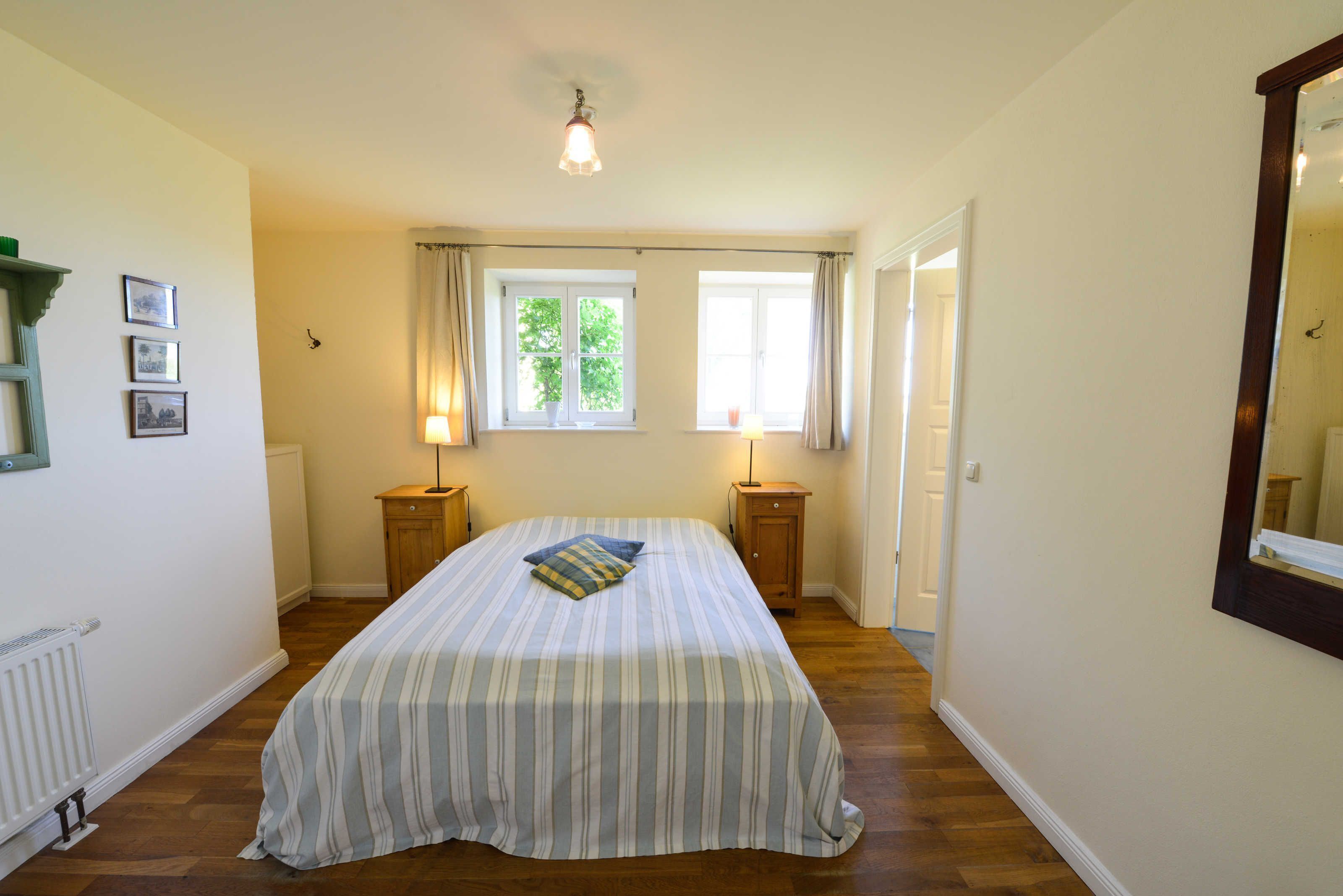 A bedroom with a large bed, two bedside tables, a window with curtains, and a ceiling light.