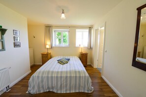 A bedroom with a large bed, two bedside tables, a window with curtains, and a ceiling light.