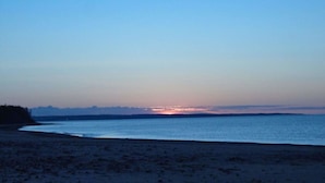 A beach at dusk with a calm sea and a distant sunset. - Little Eden Summer Beach Home  (Canoe Cove)