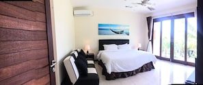 A hotel room with a large bed, a nightstand, a desk, a chair, a window with a view of the outdoors, and a ceiling fan.