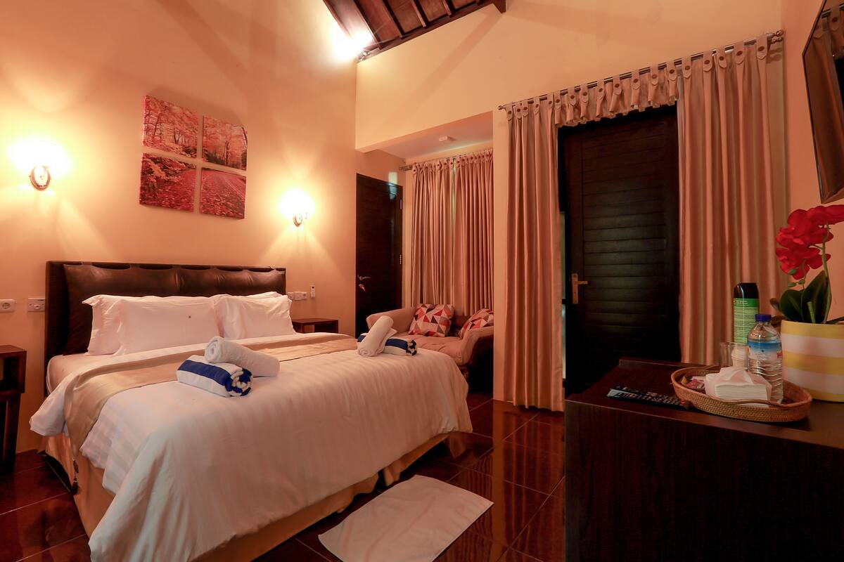 A hotel room with two beds, a desk with a remote control, a vase with flowers, and a door with curtains.