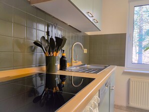 A kitchen with a black countertop, a stainless steel sink, and a window with a view of trees.