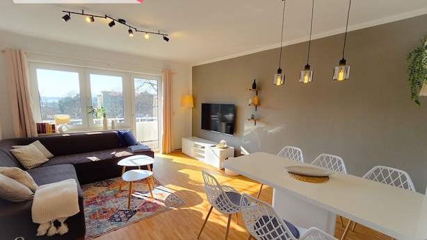 Uma sala de estar moderna com sofá, televisão, mesa de jantar e cadeiras.