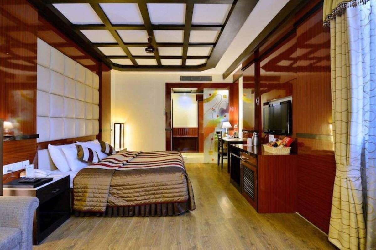 A hotel room with a bed, bedside table, lamp, TV, and a desk with a chair.