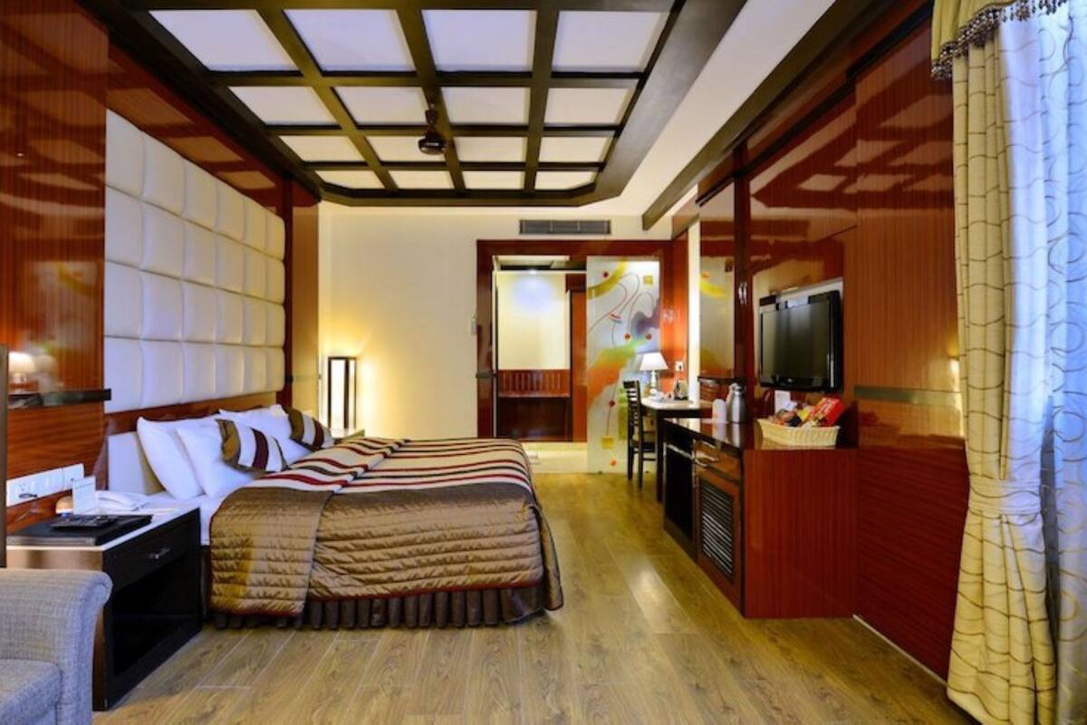 A hotel room with a large bed, a desk with a TV, and a kitchenette.