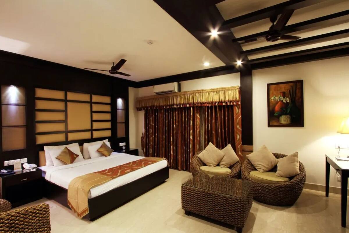 A hotel room with a large bed, two wicker chairs, a nightstand, and a ceiling fan.