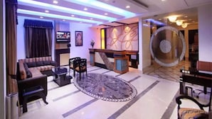 Een moderne lobby met een bank, stoelen, een bijzettafeltje, een vloerkleed met patroon, een receptiebalie en een decoratieve wand.