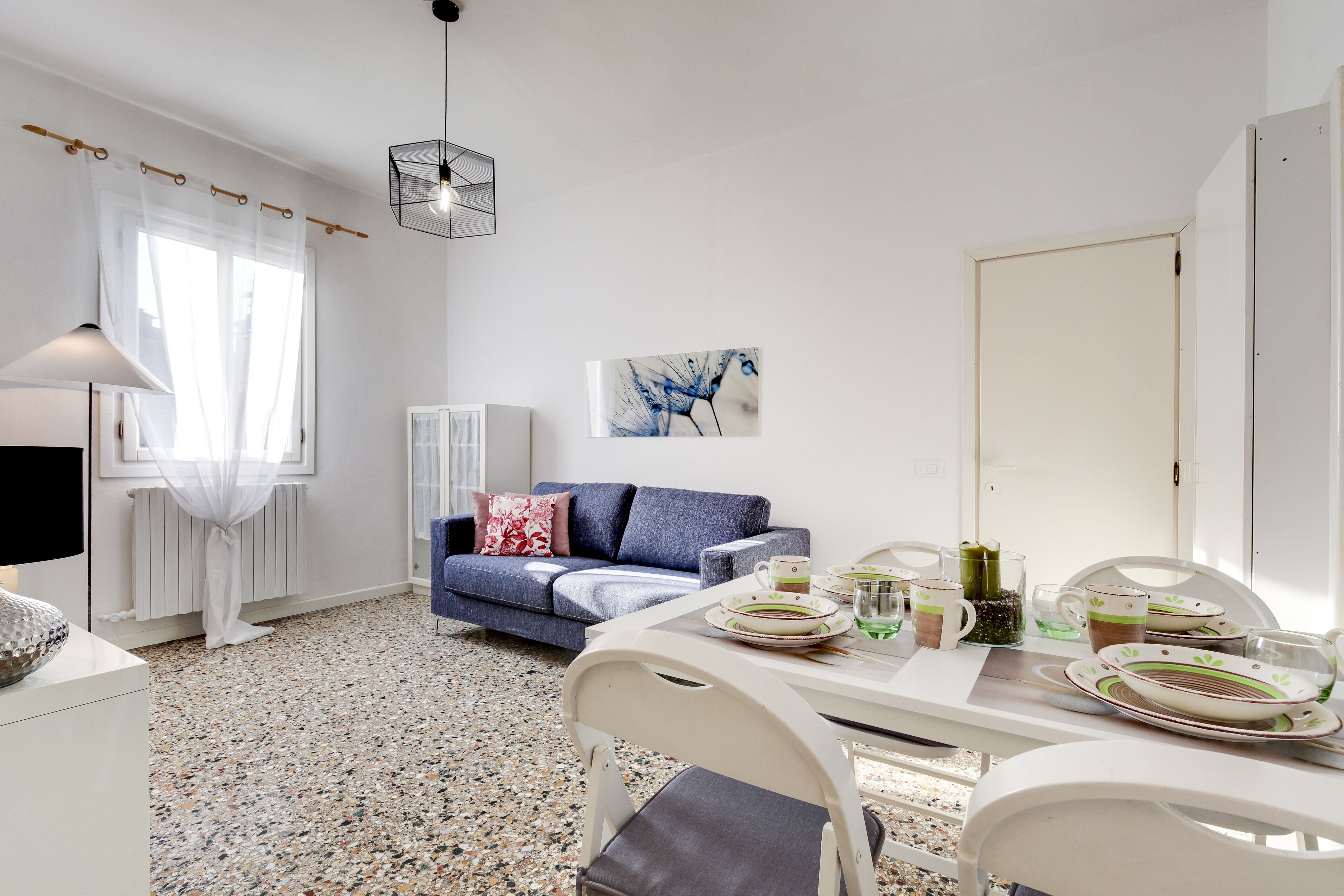 A modern living room with a blue sofa, white dining table, and a white radiator.