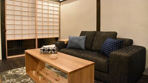 A living room with a sofa, cushions, a wooden coffee table, and a shoji screen. - Chika Miyabi (Kyoto)