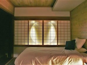 Un dormitorio japonés tradicional con suelo de tatami, una cama de madera baja y paneles shoji.