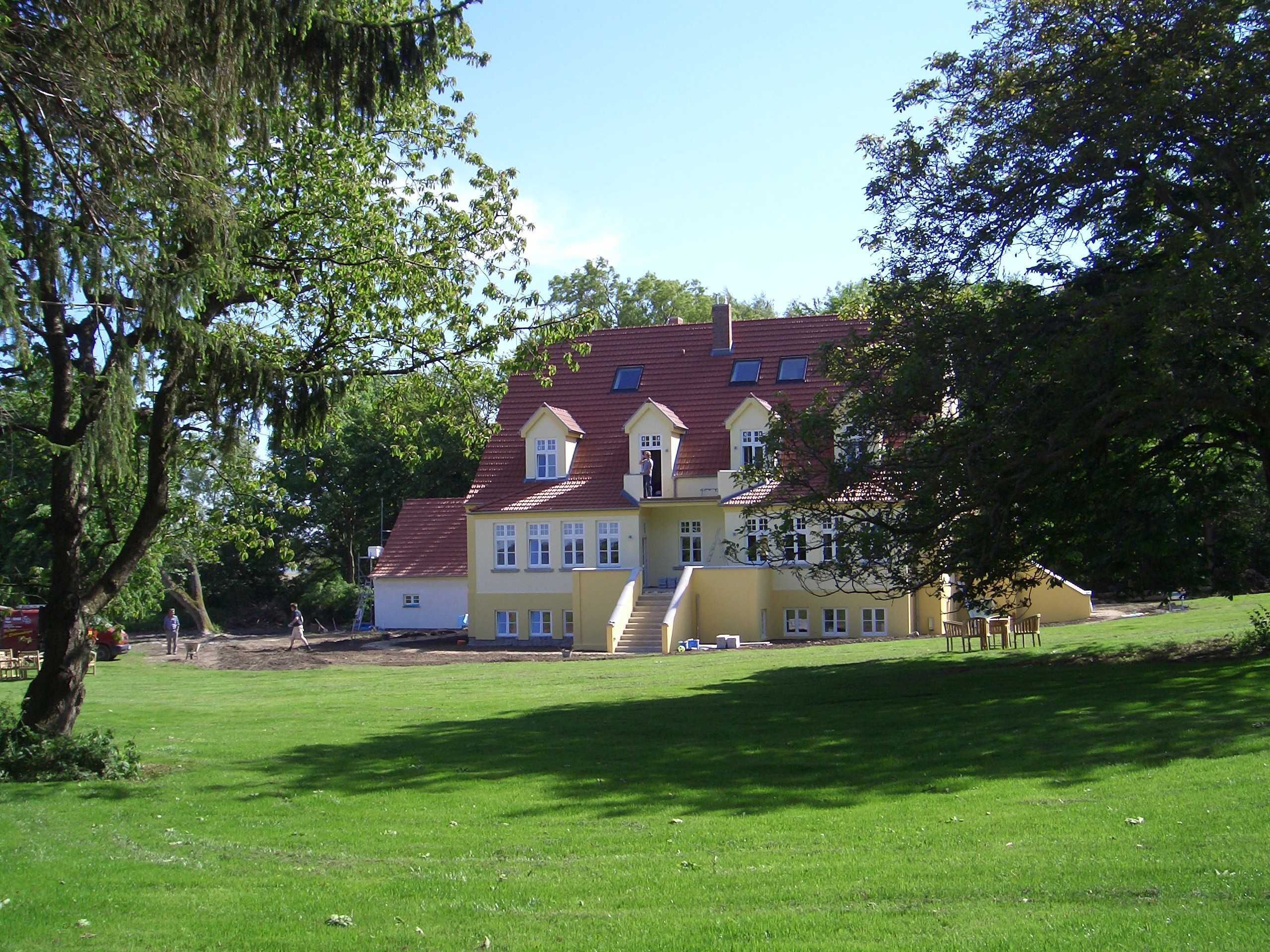 A large, yellow building with a red roof, surrounded by a well-maintained lawn and trees.