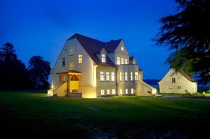 A large, multi-story house with a prominent entrance and a smaller building attached to it. - Apartment 2 for 4 persons at the water - Gut Grubnow Rügen (Neuenkirchen)